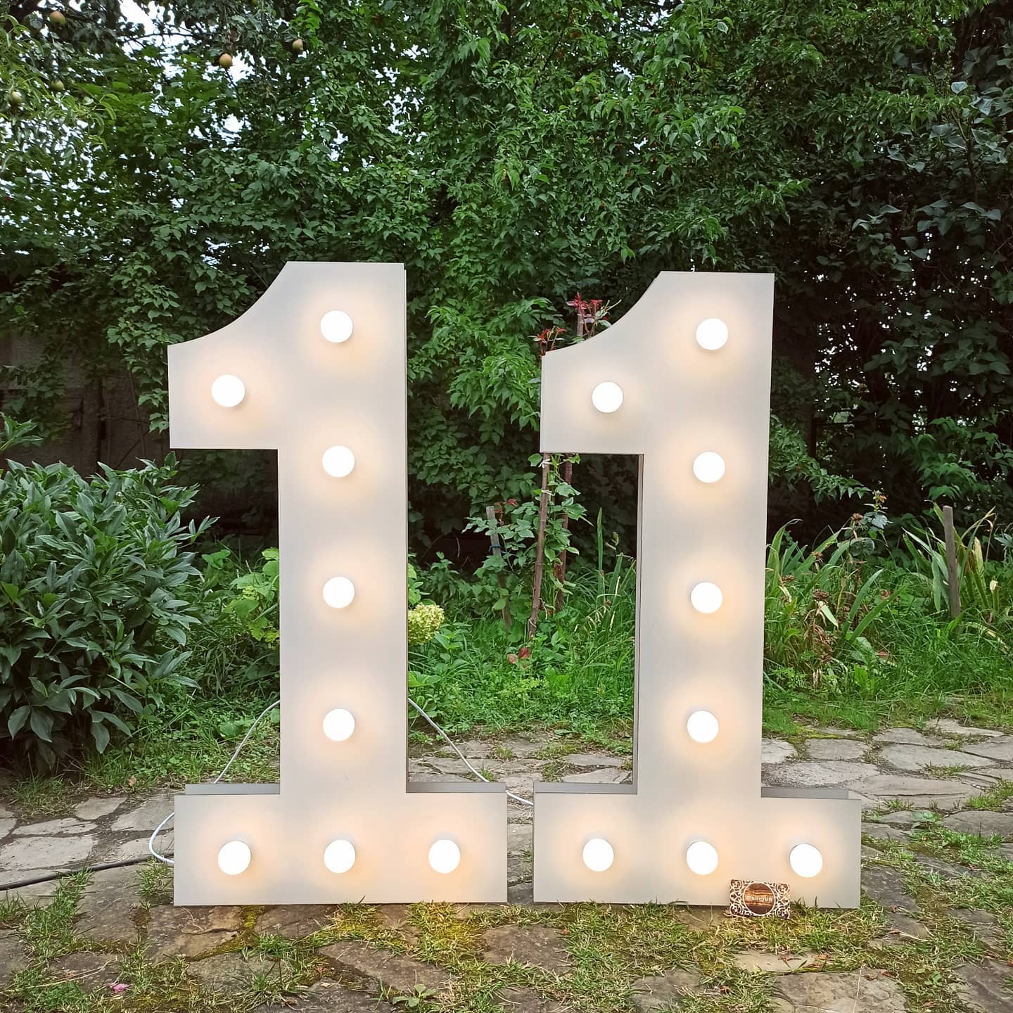 Large illuminated numbers '11' in a garden setting with greenery.