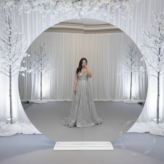 Woman in a silver dress standing in front of a circular mirror backdrop with a decorative background.