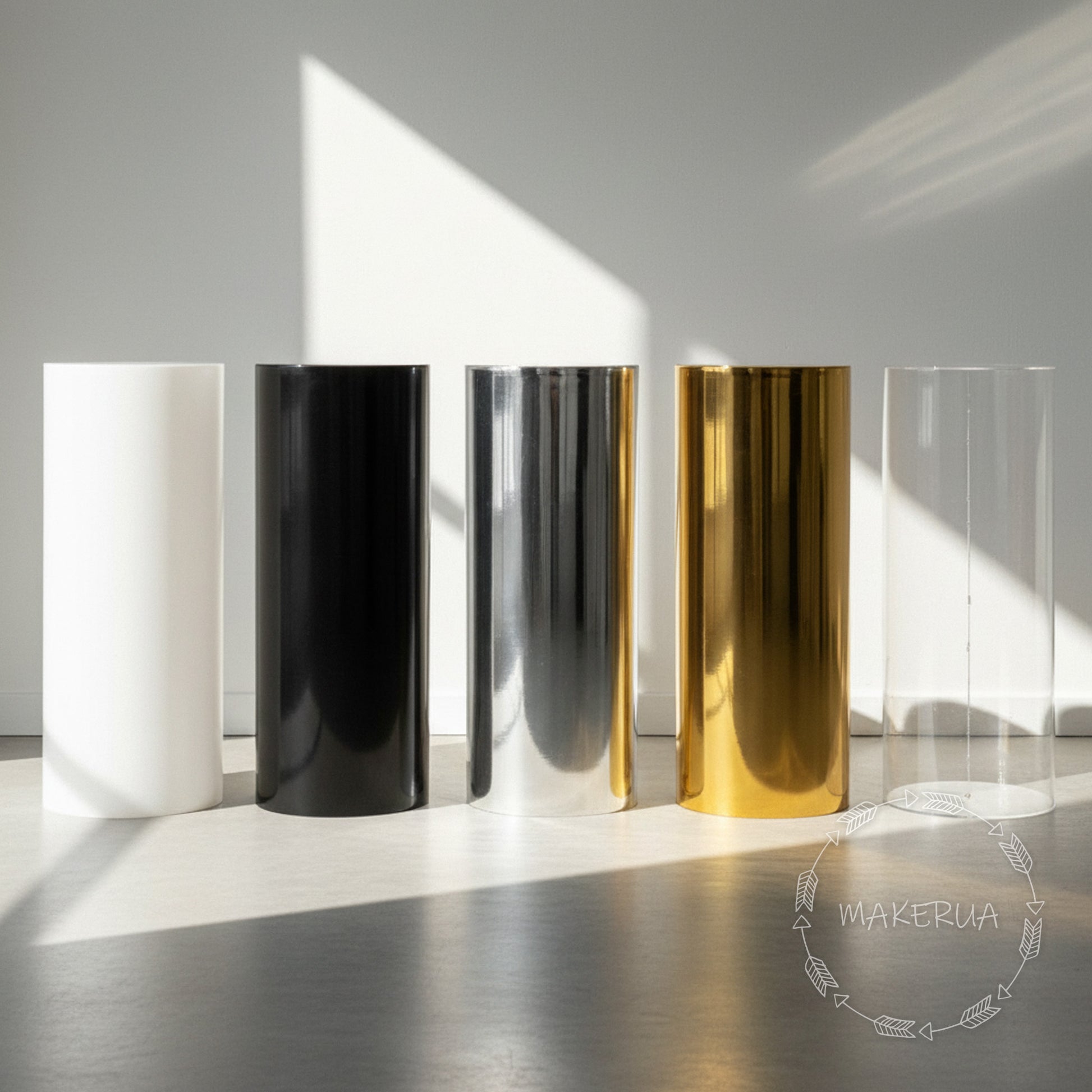Five plinth stand column cylinder pedestal display pillar in different colors (white, black, silver, gold, clear) on a reflective surface with a blurred background by MakerUA.