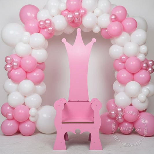 Pink wooden throne chair with a crown backrest, styled in front of a matching pink and white balloon arch. Cute seating prop for girls birthday parties, sweet 16, and baby showers.
