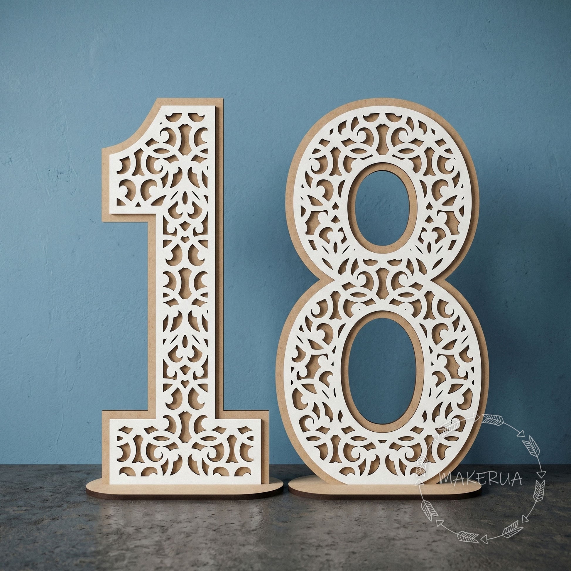 Two-layered freestanding white laminated HDF numbers 18 with intricate laser-cut lace and filigree pattern on a wooden stand against a blue studio background.