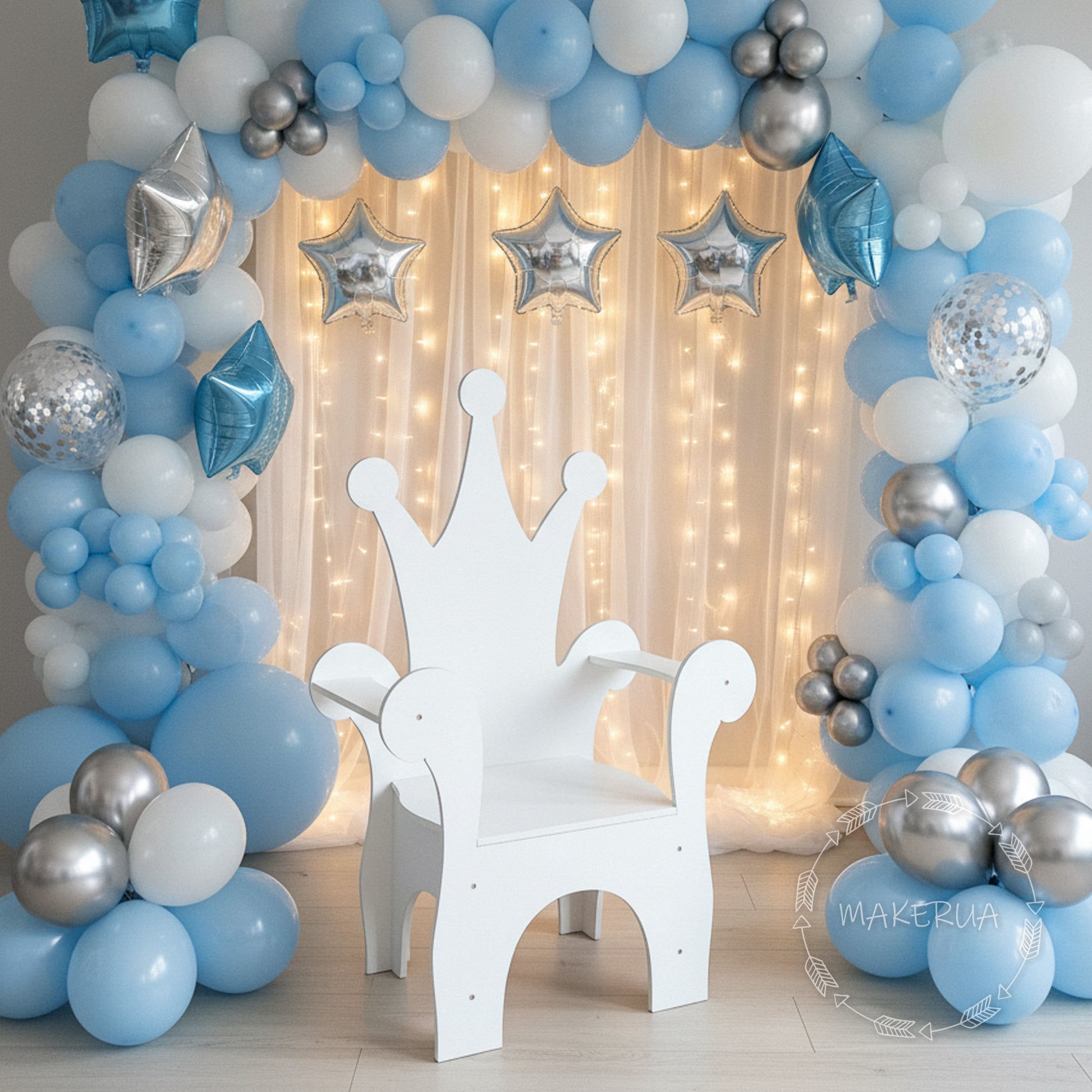 Decorative balloon arch with blue, silver, and white balloons and a white chair with a crown design in front.